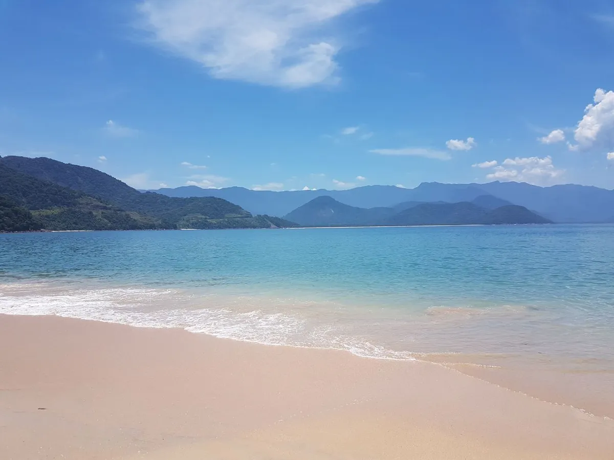 Praia da Ilha do Prumirim em Ubatuba com areia branca e água cristalina, Serra do Mar ao fundo