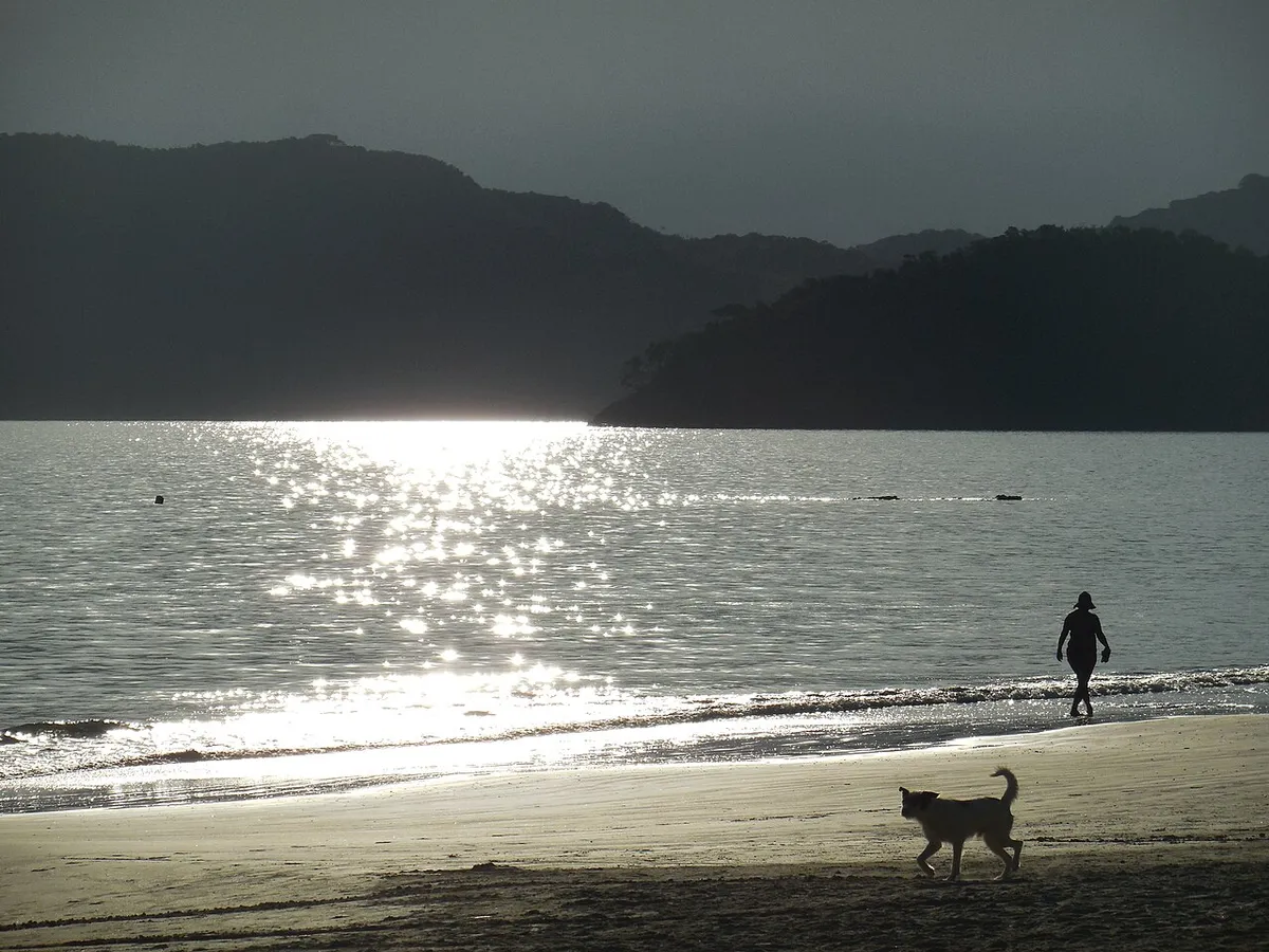 Fim de tarde na Praia da Almada em Ubatuba com mar calmo e morros ao fundo