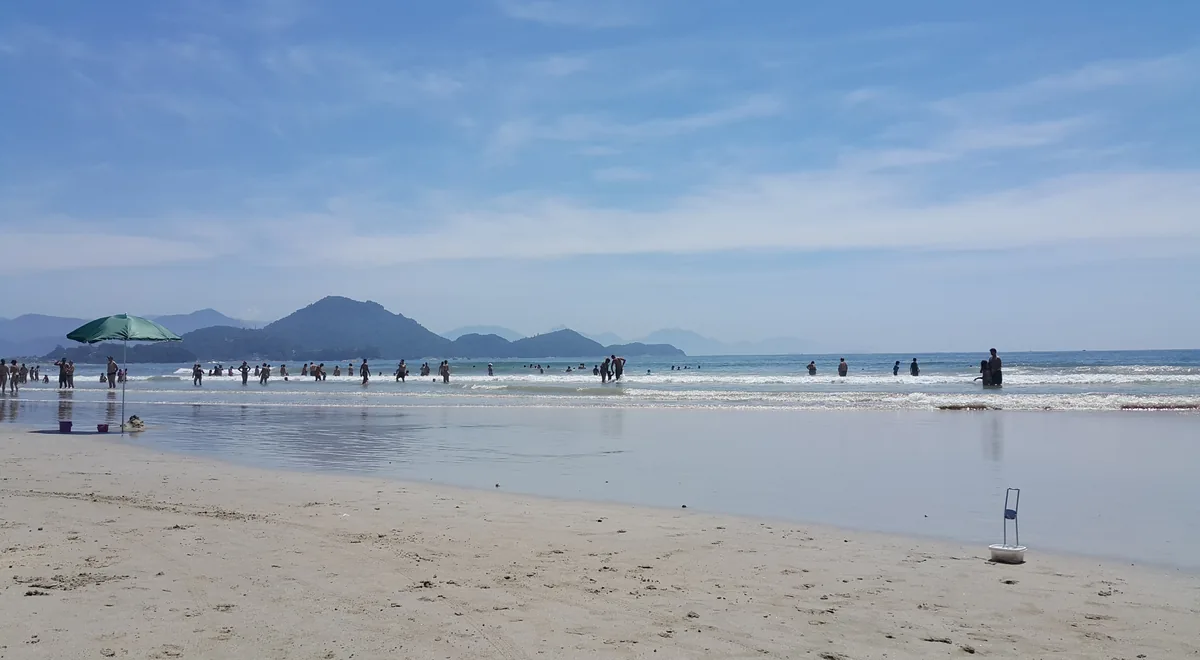 Praia das Toninhas em Ubatuba com faixa de areia, mar aberto e o Morro da Ponta Grossa ao fundo