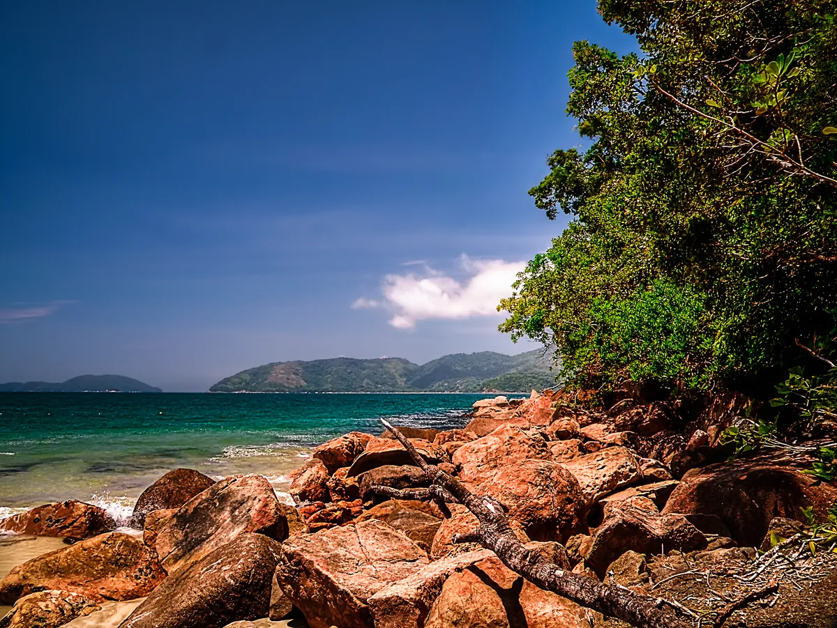 Praia do Lázaro em Ubatuba com mar verde-turquesa, pedras na orla e Mata Atlântica ao fundo